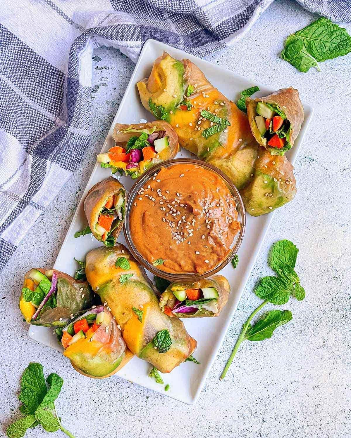 Veggie Summer Rolls with Peanut Butter Dipping Sauce in a plate with some cut in half showing veggies
