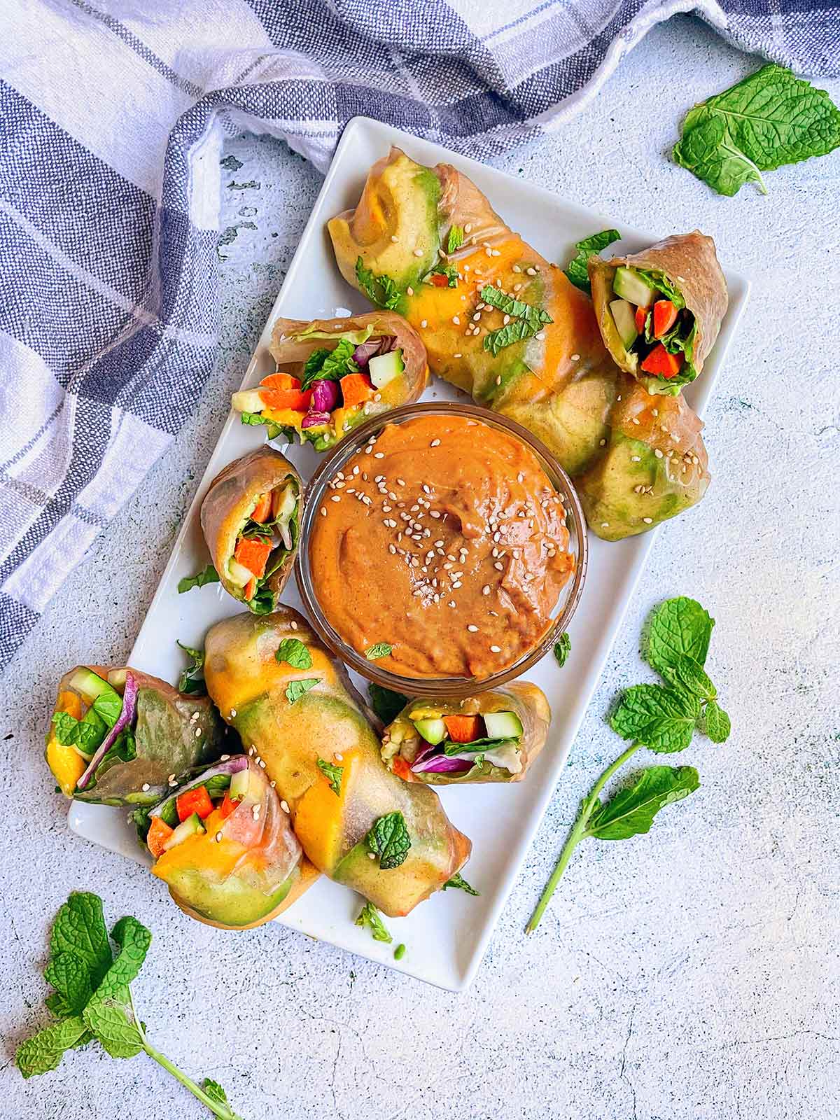 Veggie Summer Rolls with Peanut Butter Dipping Sauce in a plate with some cut in half showing veggies