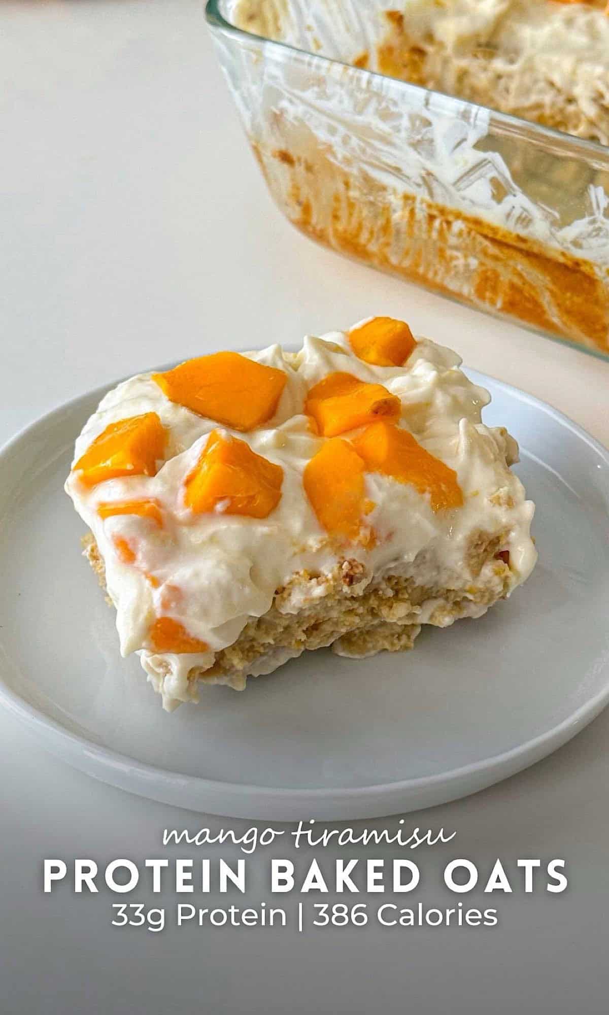 Mango Tiramisu Protein Baked Oats 10 A square slice of mango tiramisu protein baked oats on a white plate, topped with creamy yogurt and fresh mango chunks. The remaining tray of baked oats is visible in the background.