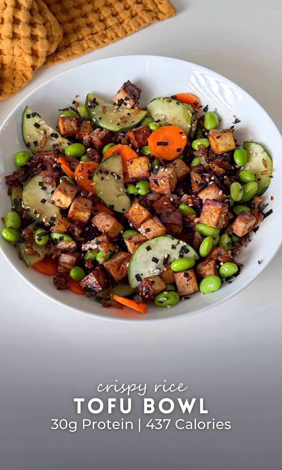 Viral Crispy Rice Tofu Bowl 10 White bowl filled with a crispy rice tofu bowl, topped with golden tofu cubes, sliced cucumbers, carrots, edamame, and sprinkled with sesame seeds and seaweed flakes.