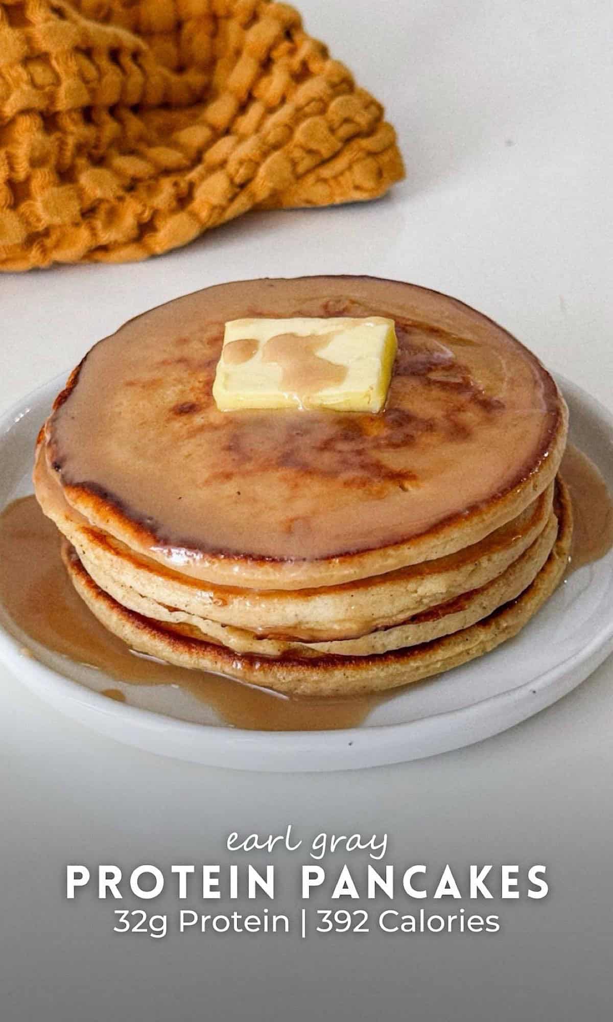 Earl gray pancakes stacked on a small white plate, made with tea-infused batter for a subtle floral flavor, topped with a pat of butter and drizzled with maple syrup. The pancakes are golden brown with syrup pooling around the edges, styled on a white surface with a textured mustard cloth in the background.