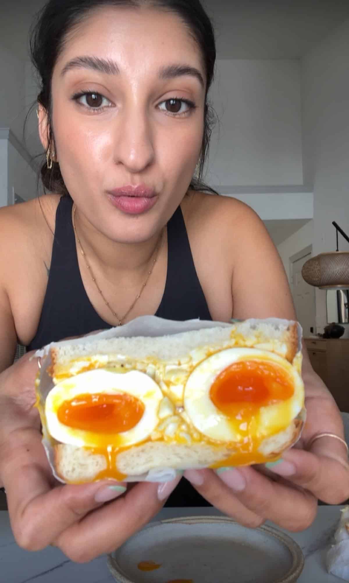Japanese egg sandwich held in hand, made with soft white bread filled with creamy egg salad and halved soft-boiled eggs with jammy yolks oozing out.