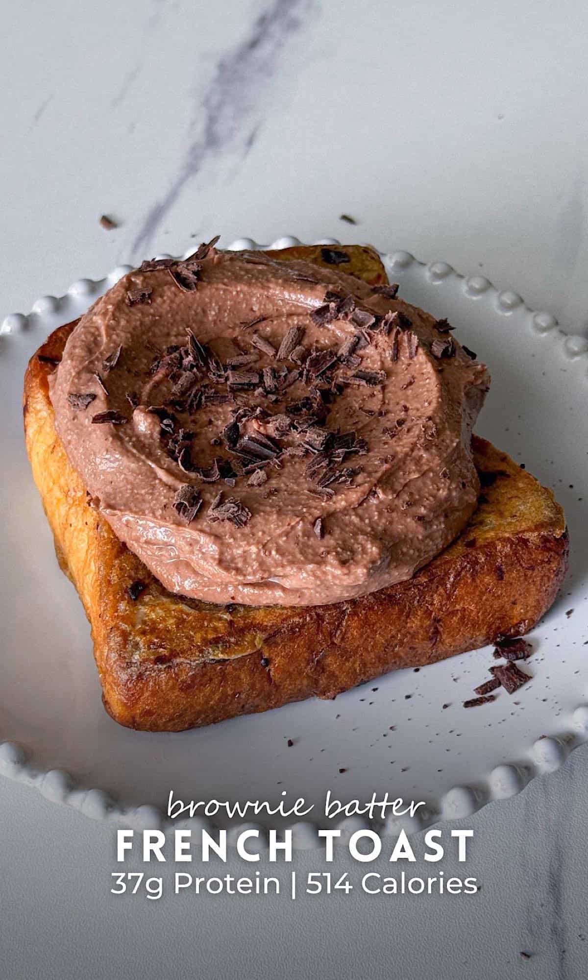Slice of brownie batter French toast on a white plate, topped with a thick, creamy chocolate brownie batter spread and finished with chocolate shavings.