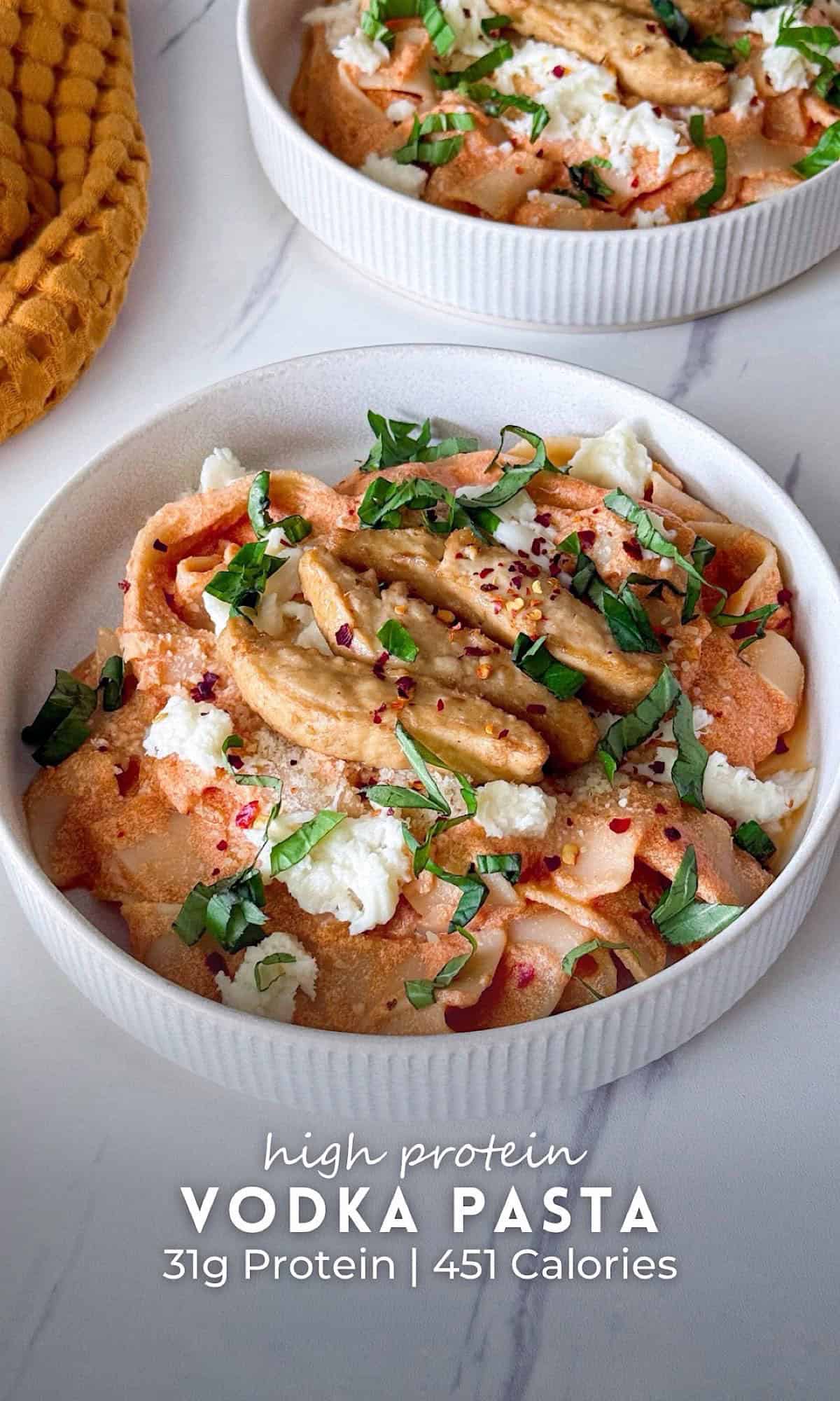 Two bowls of high protein vodka pasta with creamy tomato sauce, topped with cottage cheese, grated parmesan, fresh basil, red pepper flakes, and pieces of protein pasta.