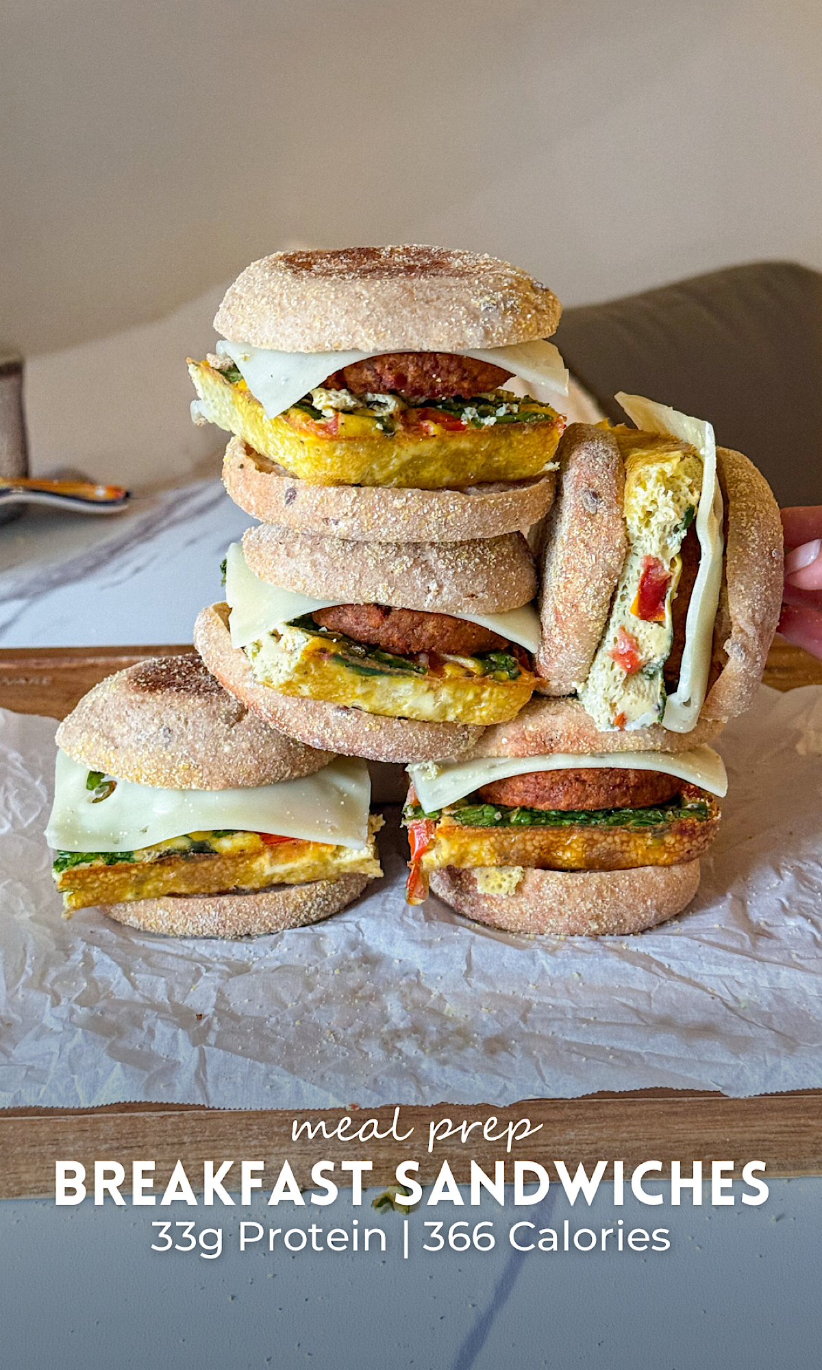 Meal Prep Breakfast Sandwiches 9 Stack of meal prep breakfast sandwiches made with English muffins, fluffy veggie egg patties, vegetarian sausage, spinach, and melted cheese on a wooden board with one sandwich cut open to show the filling.