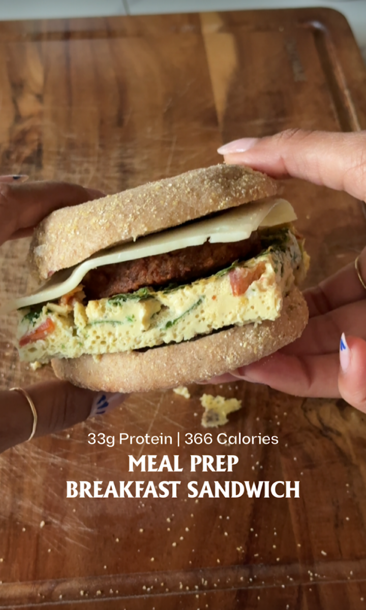 Meal Prep Breakfast Sandwiches 5 Stack of meal prep breakfast sandwiches made with English muffins, fluffy veggie egg patties, vegetarian sausage, spinach, and melted cheese on a wooden board with one sandwich cut open to show the filling.