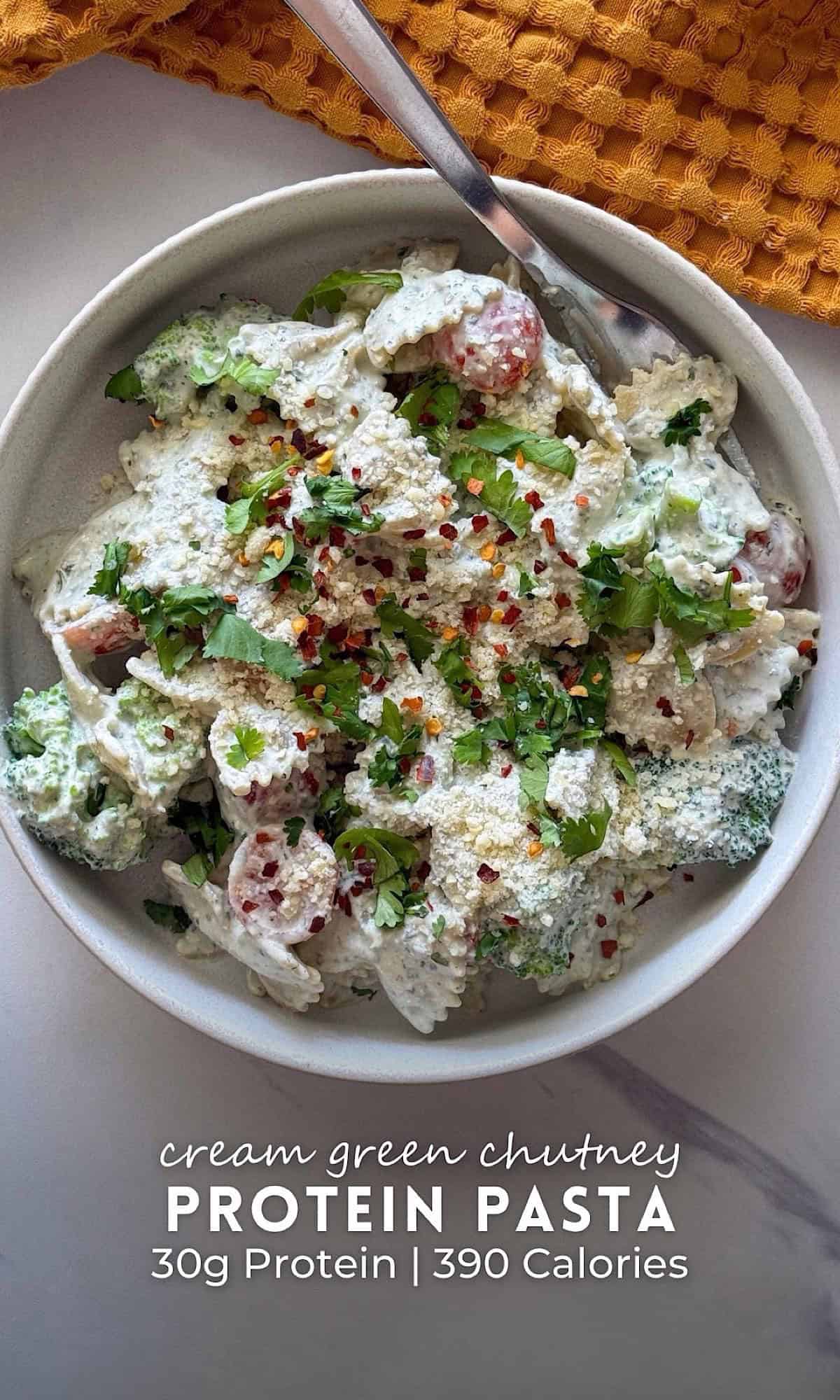 Creamy Green Chutney Protein Pasta 9 Creamy green chutney protein pasta made with bowtie pasta, broccoli, and tomatoes tossed in a rich herb-packed yogurt sauce, then topped with grated parmesan, cilantro, and red pepper flakes in a white bowl.