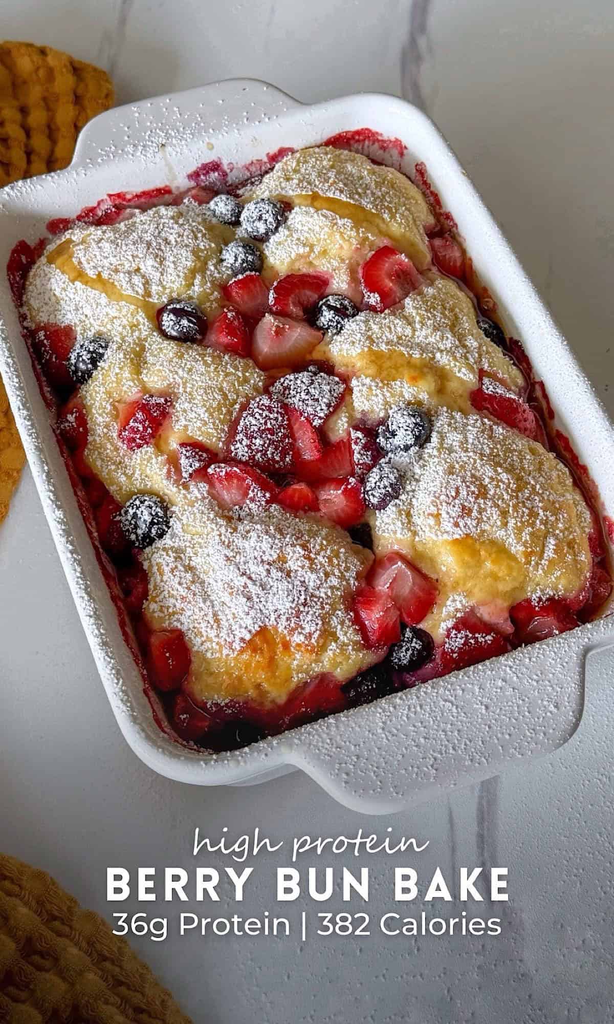 High Protein Berry Bun Bake 10 High protein berry bun bake served in a white ceramic baking dish, featuring juicy strawberries and blueberries baked beneath fluffy golden biscuit-style topping. The warm berry filling bubbles around the edges and is finished with a generous dusting of powdered sugar for a cobbler-inspired breakfast bake.