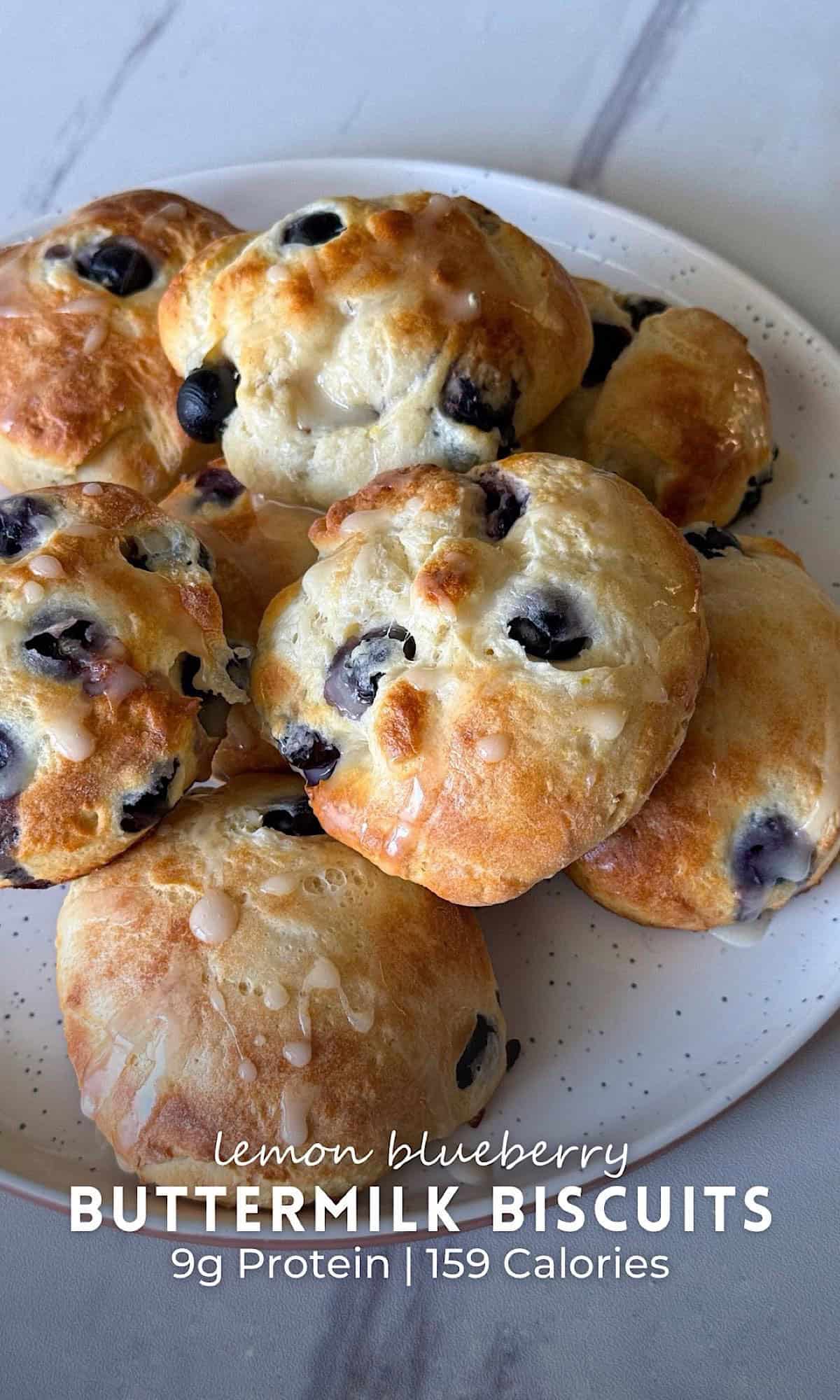 Lemon blueberry buttermilk biscuits baked until golden brown and filled with juicy blueberries, finished with a sweet lemon glaze and arranged on a white plate.