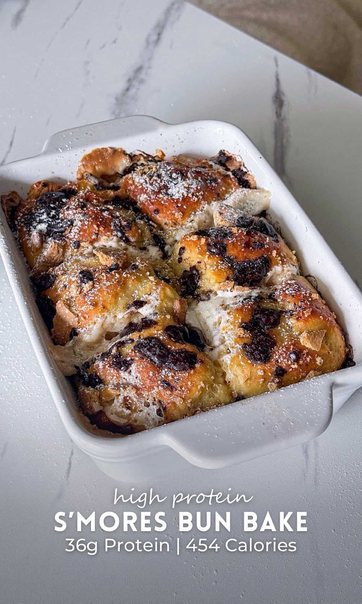 High Protein S’mores Bun Bake 10 High protein s’mores bun bake with golden buns, melted marshmallow, chocolate chunks, and crushed graham crackers, finished with powdered sugar in a white baking dish.