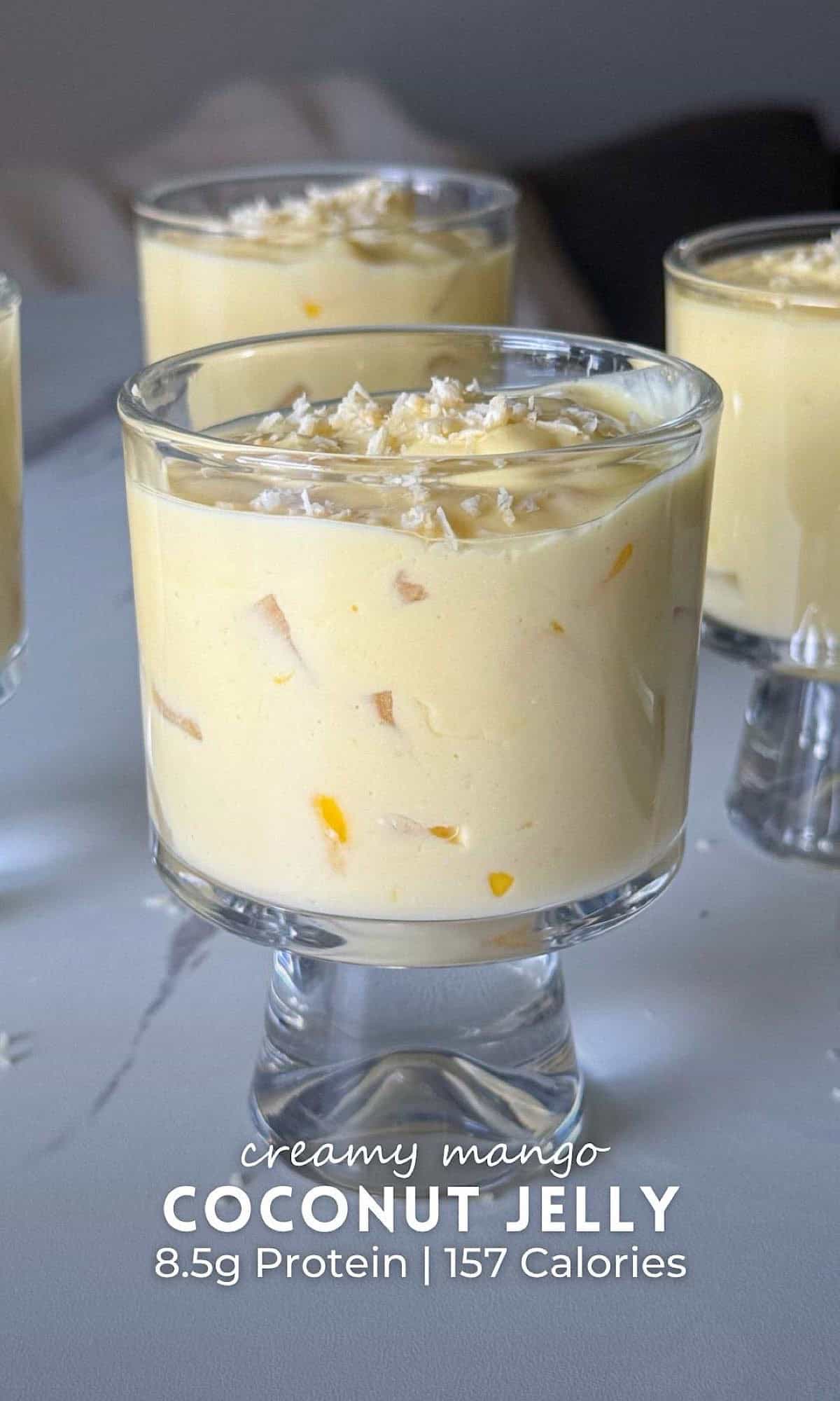 Creamy mango coconut jelly served in glass dessert cups with chunks of fresh mango and coconut jelly, topped with shredded coconut.