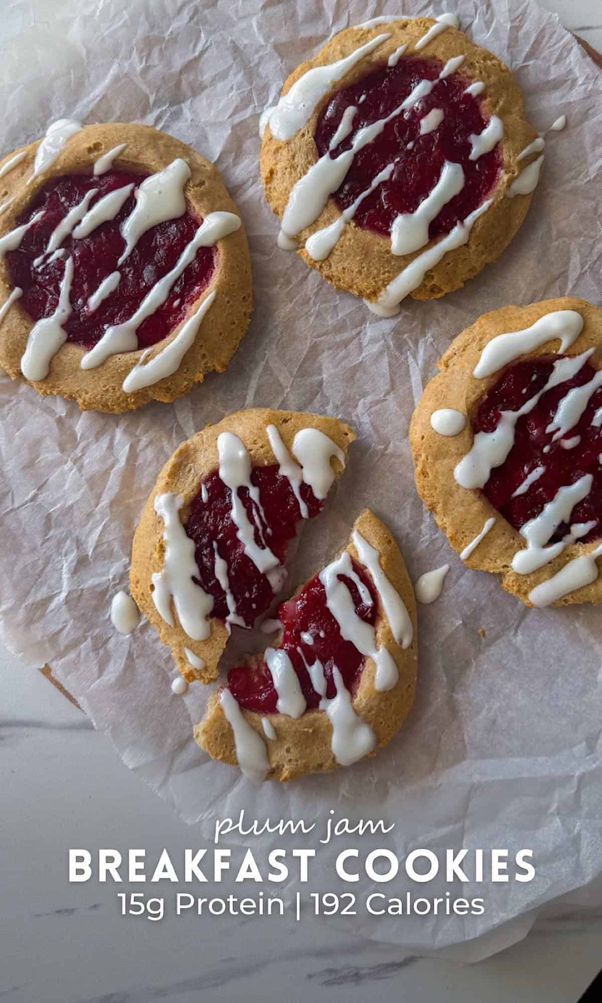 Plum jam breakfast cookies filled with homemade plum jam and drizzled with creamy white icing, arranged on parchment paper.