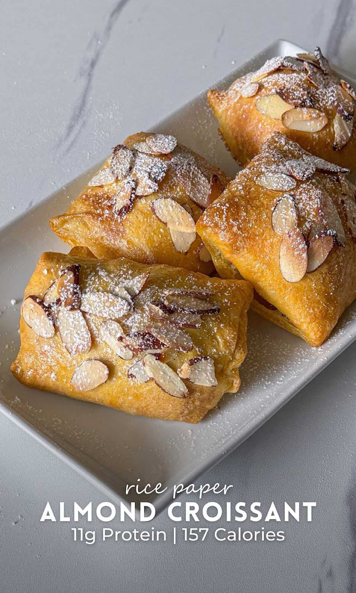Rice Paper Almond Croissants | Air Fryer Recipe 9 Rice paper almond croissants filled with frangipane, topped with toasted sliced almonds and powdered sugar, arranged on a white rectangular plate.