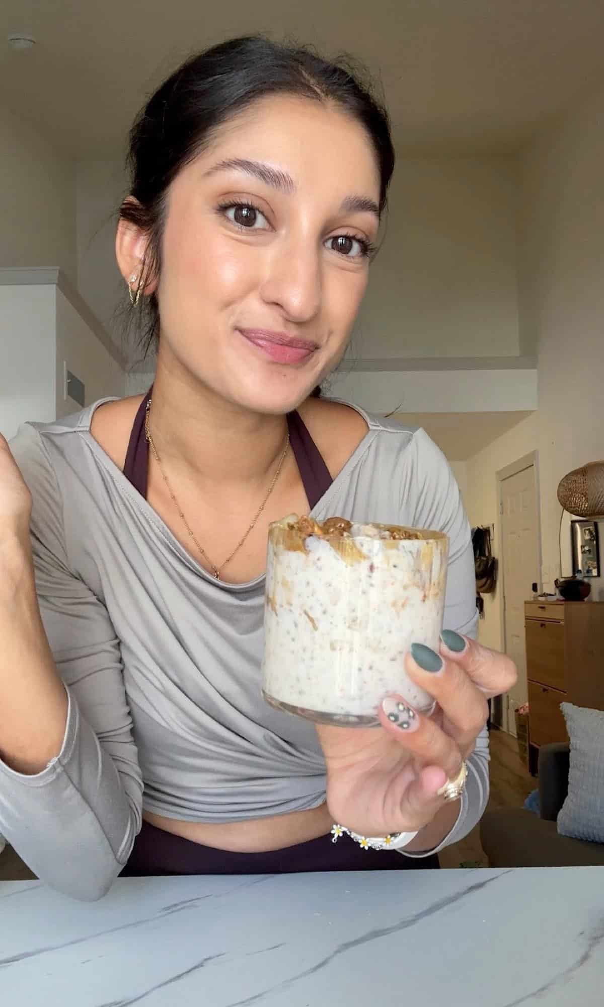 High Protein Caramel Apple Oatmeal 2 A woman smiling at the camera while holding a glass of oatmeal.